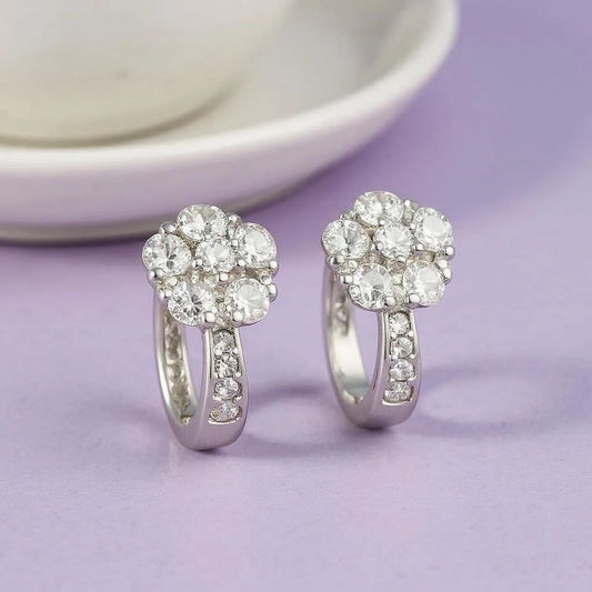 Pair of silver earrings with clear gemstones on a light purple background