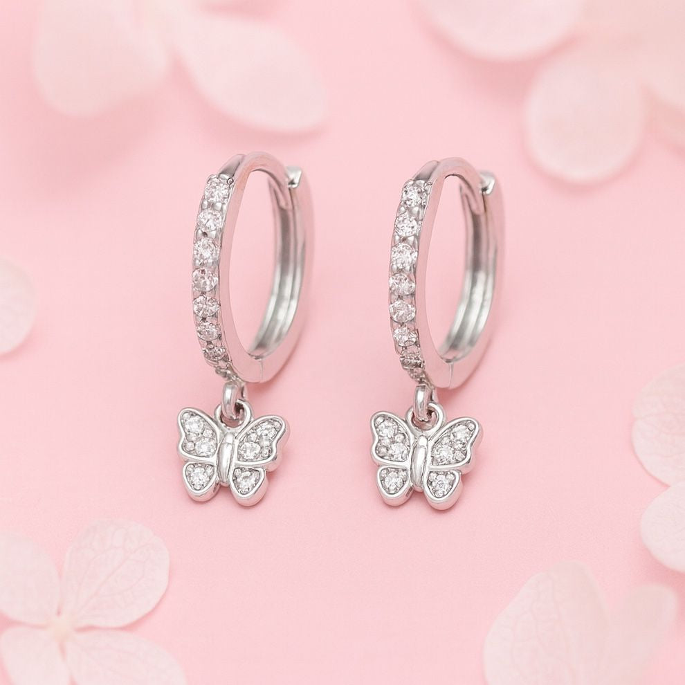 Silver hoop earrings with butterfly charms on a pink floral background
