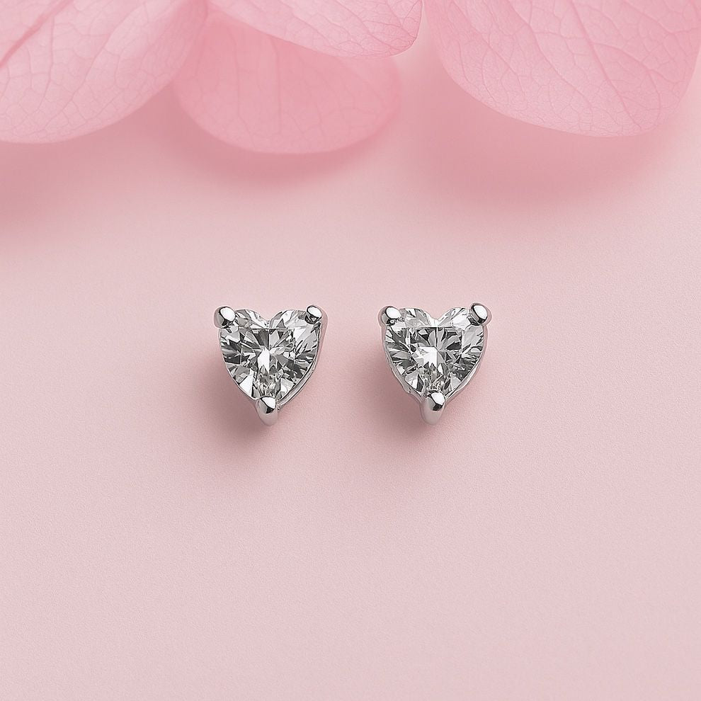 Heart-shaped tiny silver earrings on a soft pink background