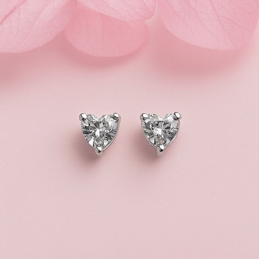 Heart-shaped tiny silver earrings on a soft pink background