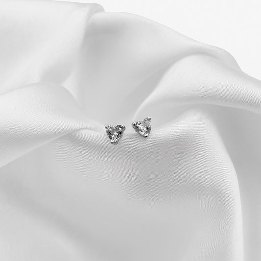 Pair of silver heart-shaped stud earrings on white fabric