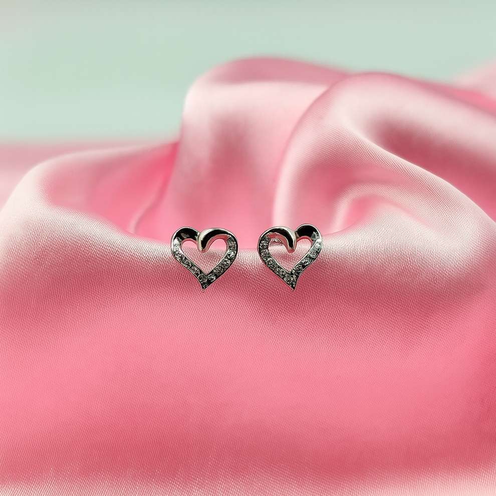 Heart-shaped silver earrings on pink satin fabric