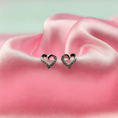 Heart-shaped silver earrings on pink satin fabric