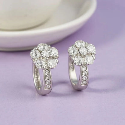 Pair of silver earrings with clear gemstones on a light purple background