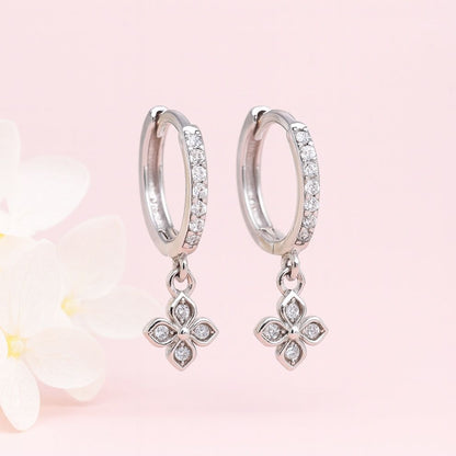 Silver hoop earrings with floral charms on a soft pink background