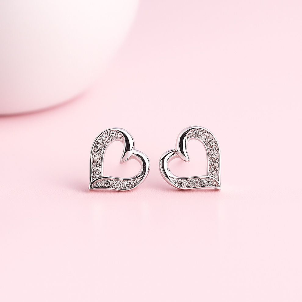 Heart-shaped silver earrings with small white stone on a pink background