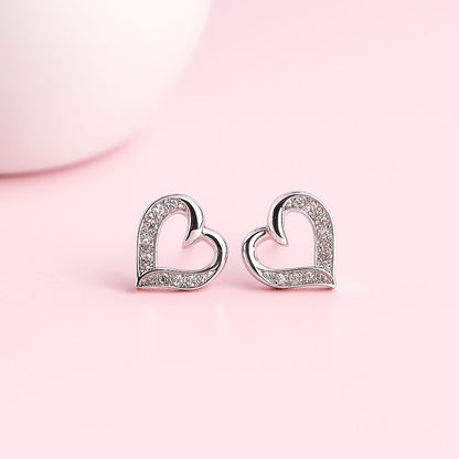 Heart-shaped silver earrings with small white stone on a pink background