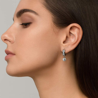 Close-up of a woman wearing silver with white stone hoop earrings against a neutral background