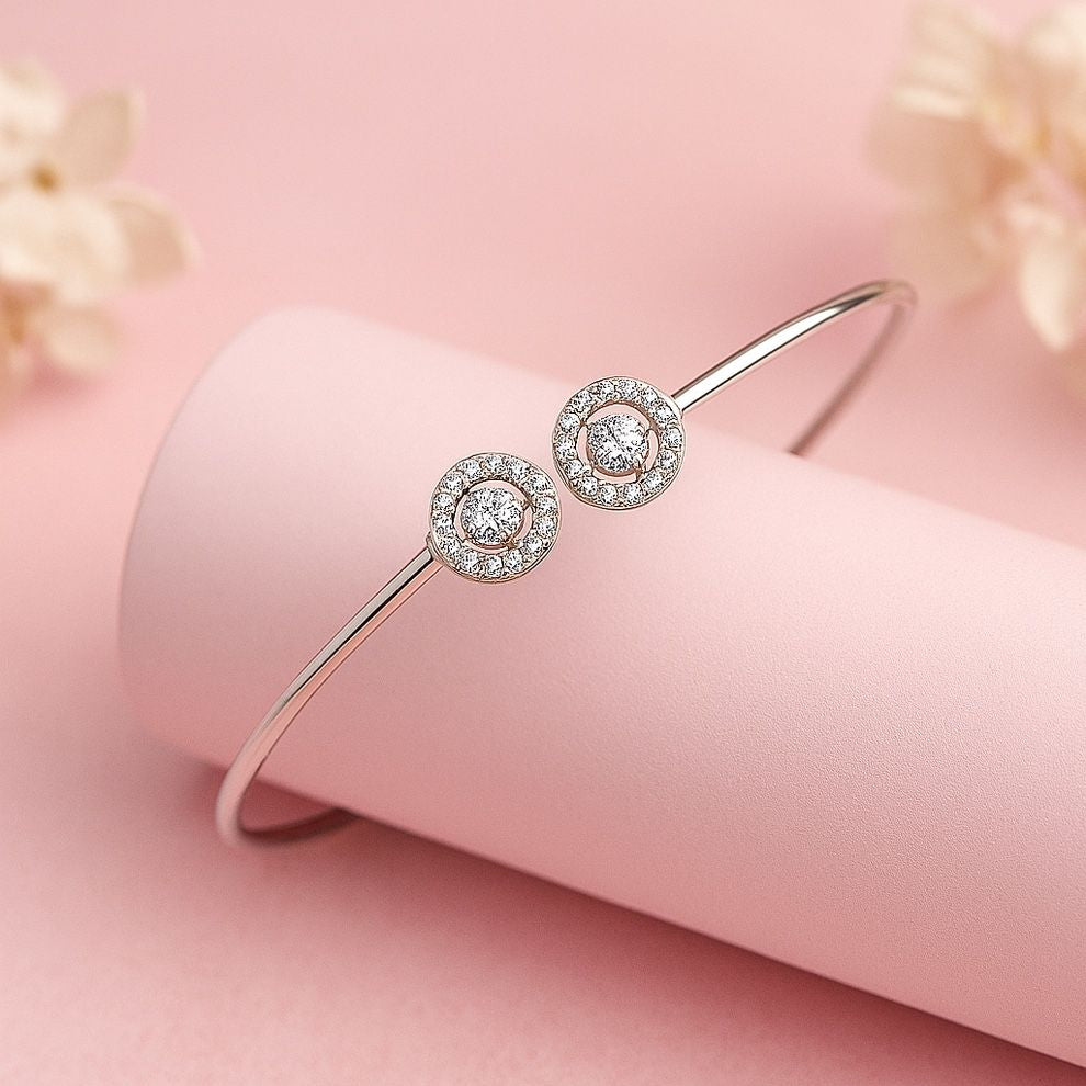 Silver bracelet with two circular diamond-like charms on a pink background