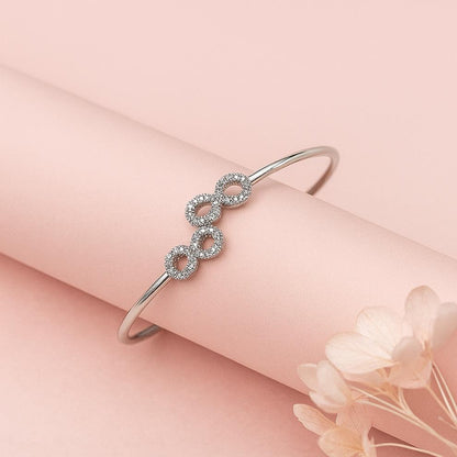 Silver bracelet with interlocking infinity loops on a pink surface with flowers