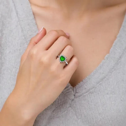 Close-up of a women hand wearing a silver ring with a green gemstone, against a neutral background.