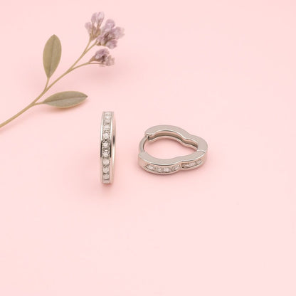 Pair of silver hoop earrings with small  white stones on a pink background