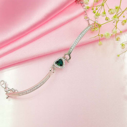 Silver bracelet with a green heart charm on a pink fabric background
