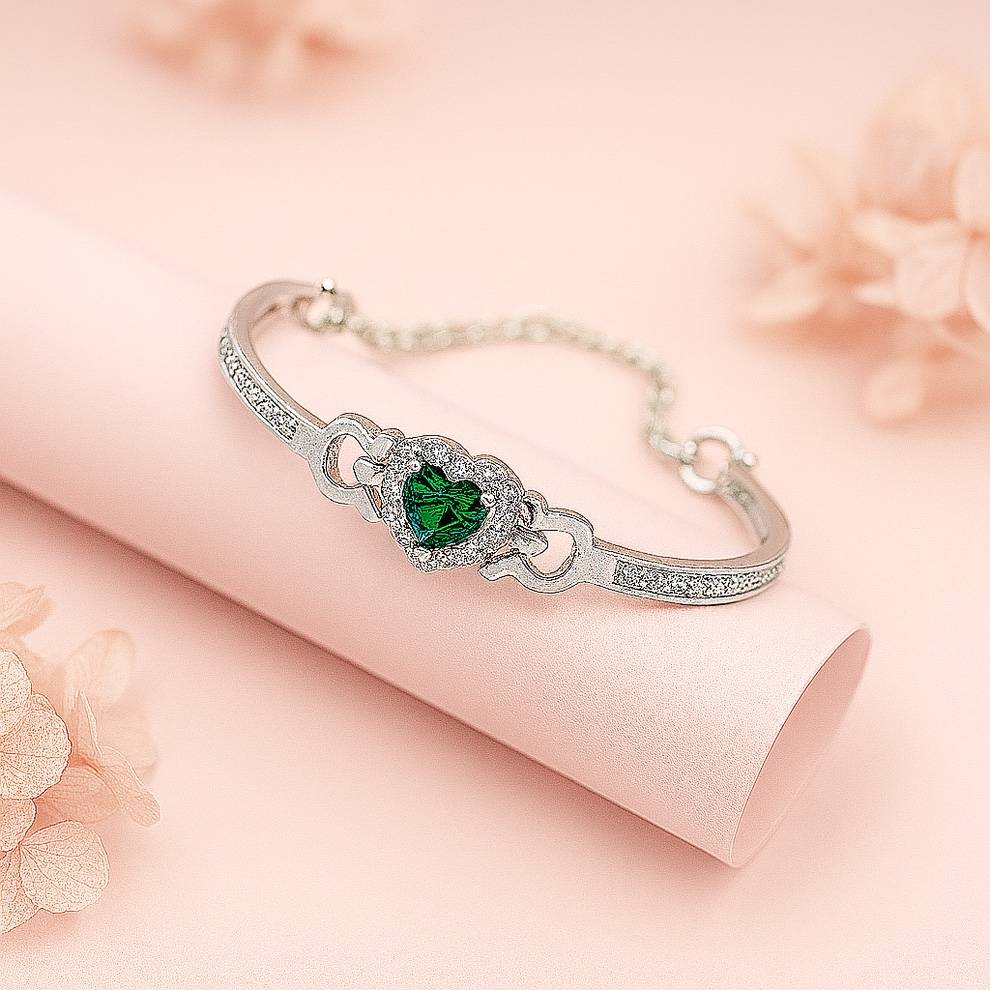 Silver bracelet with a green gemstone on a soft pink background