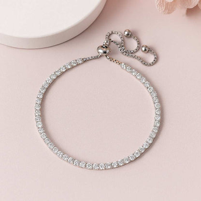 Silver tennis bracelet with clear stones on a pink surface