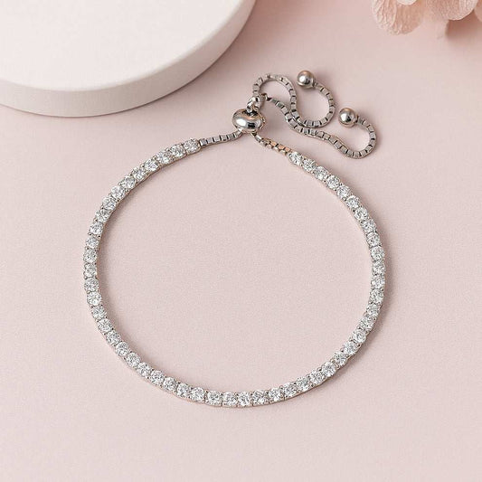 Silver tennis bracelet with clear stones on a pink surface