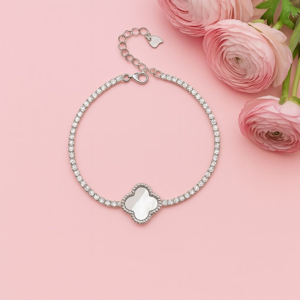 Silver bracelet with heart charm on a pink background with pink flowers