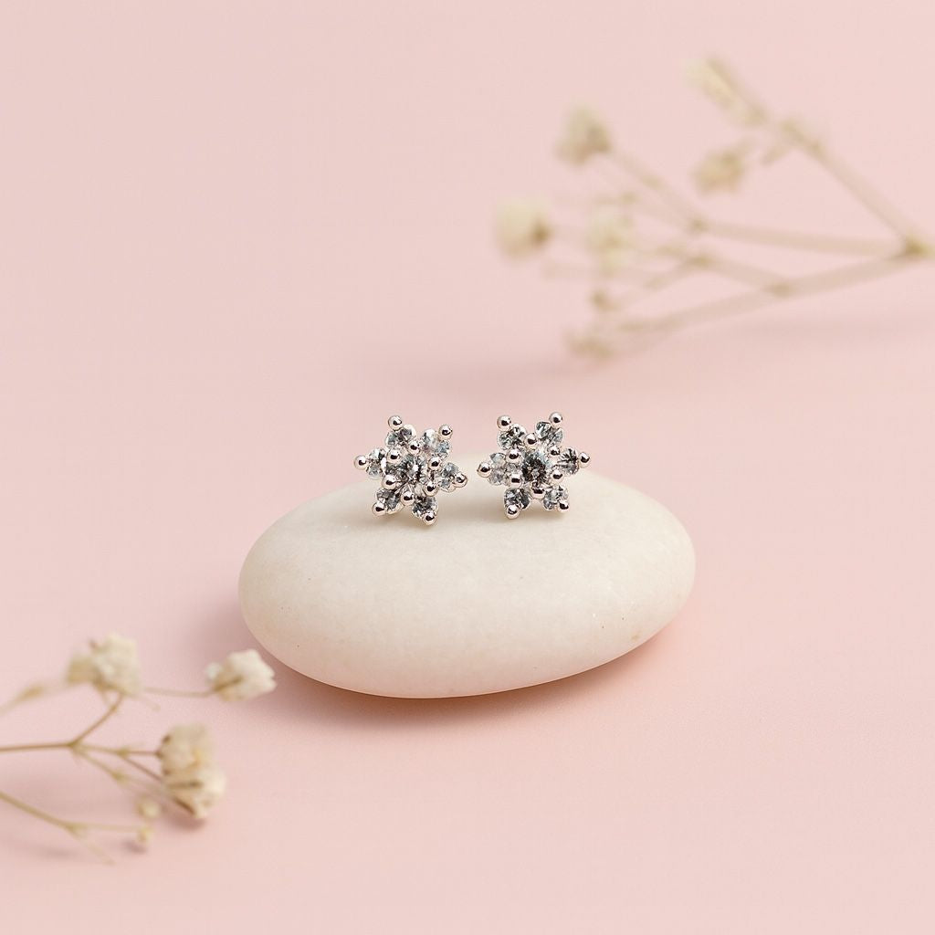 Silver star-shaped earrings on a white stone with a pink background