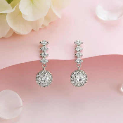 Silver earrings with clear stones on a pink floral background