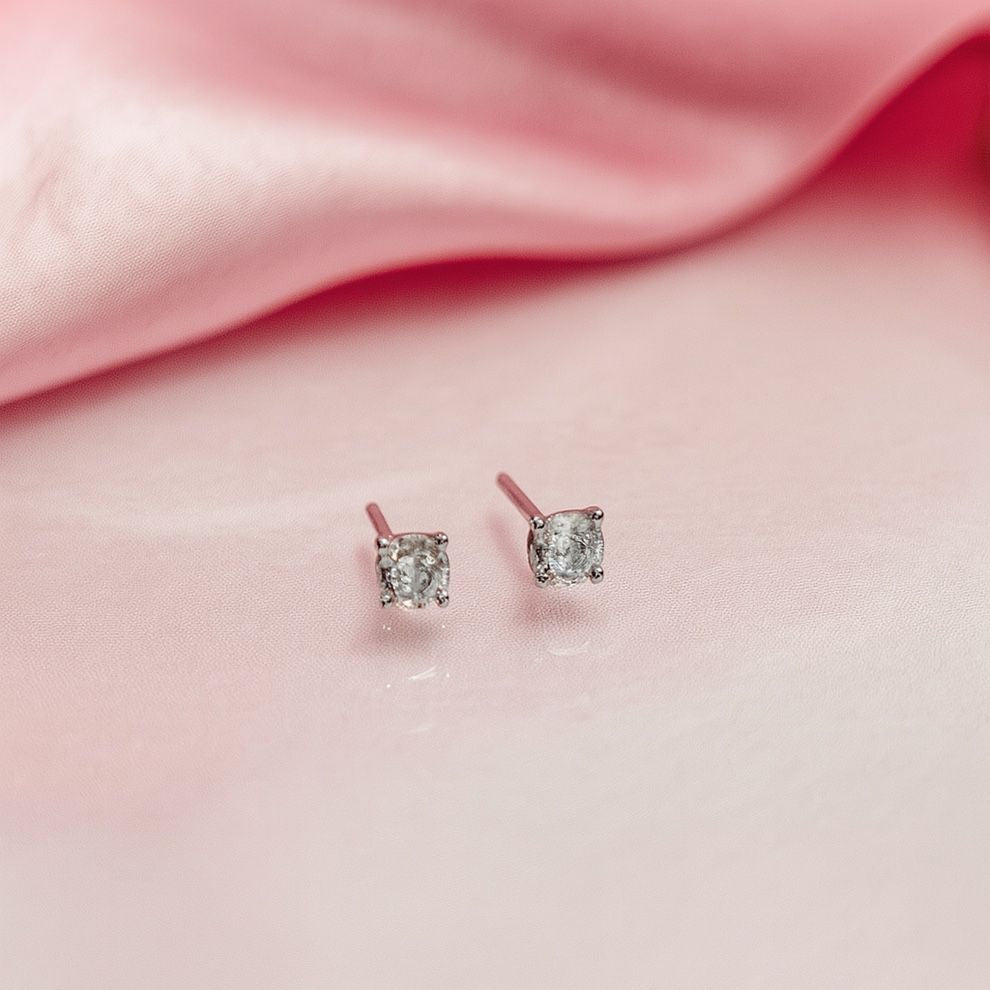 Pair of silver stud earrings on a pink fabric background