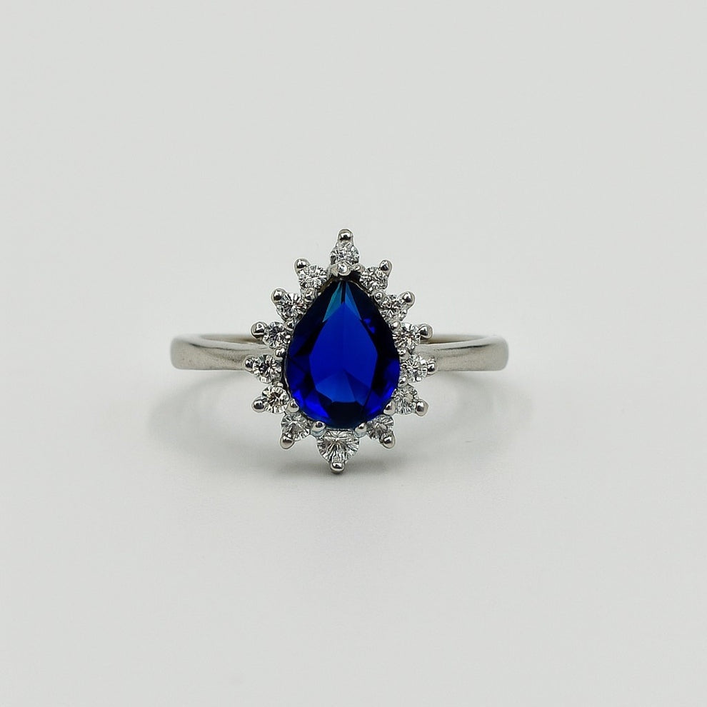 Silver ring with a blue teardrop-shaped gemstone on a light gray background