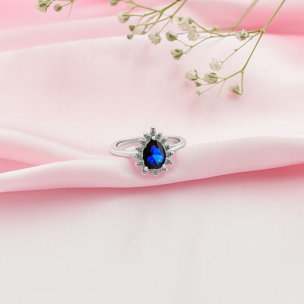 Silver ring with a blue gemstone on pink fabric
