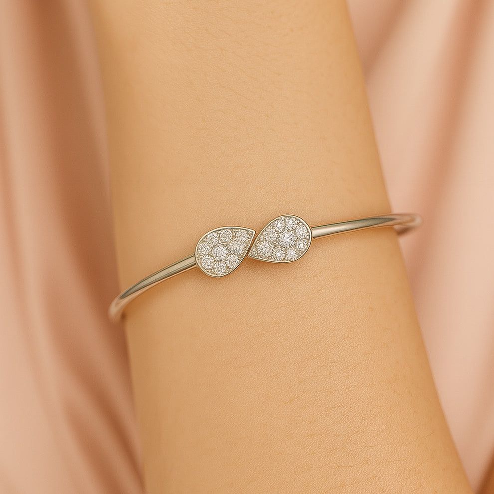 Silver bracelet with teardrop-shaped diamond accents on a wrist against a beige background