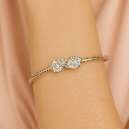 Silver bracelet with teardrop-shaped diamond accents on a wrist against a beige background